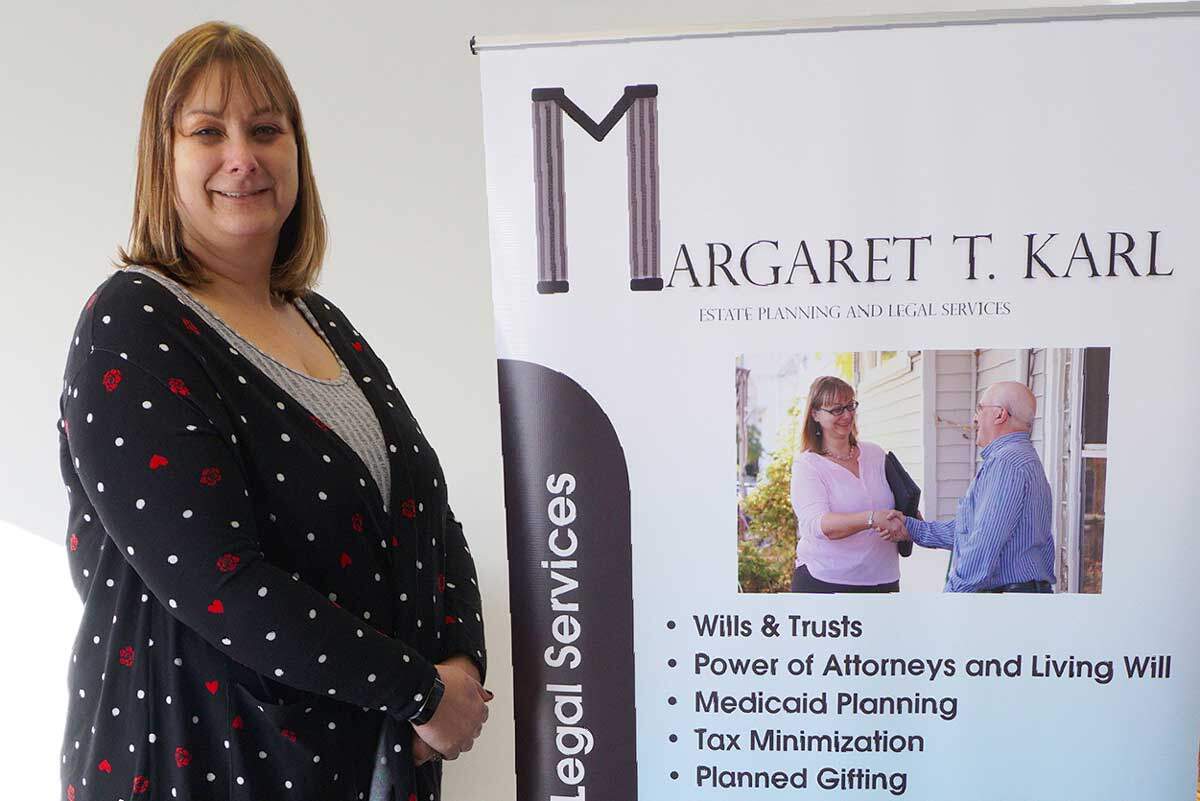Attorney Margaret Karl standing next to a poster for her business, ready to share her expertise on estate planning, elder law, and legal matters.